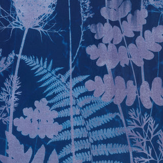 A close-up of cyanotype print featuring botanical silhouettes in light lavender and pale blue on a deep navy blue background.